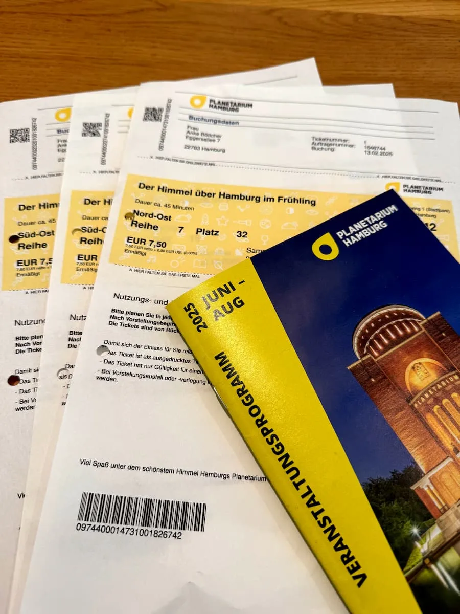 Das Veranstaltungsprogramm vom Planetarium Hamburg für Juni bis August. Dehinter drei Eintrittskarten für die Veranstaltung „der Himmel über Berlin“.